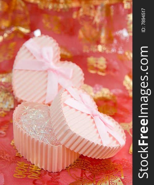 Still life of a pair of heart shaped boxes with ribbons on a red thin cloth decorated with gold Chinese characters and figures depicting marriage. Still life of a pair of heart shaped boxes with ribbons on a red thin cloth decorated with gold Chinese characters and figures depicting marriage