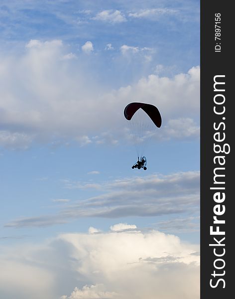 A powered paraglider pilot in flight with a cloudy sky in the background. A powered paraglider pilot in flight with a cloudy sky in the background