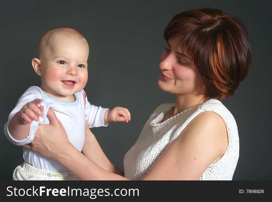 Laughing baby boy and his mother on grey background