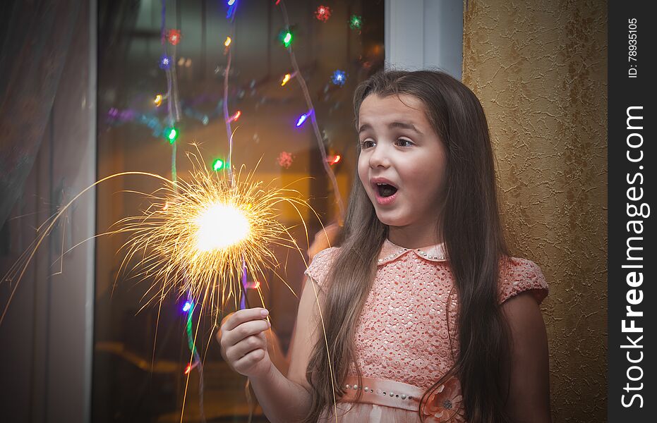 Little suprised girl with long brown hair in pink dress holding a sparkler. Little suprised girl with long brown hair in pink dress holding a sparkler