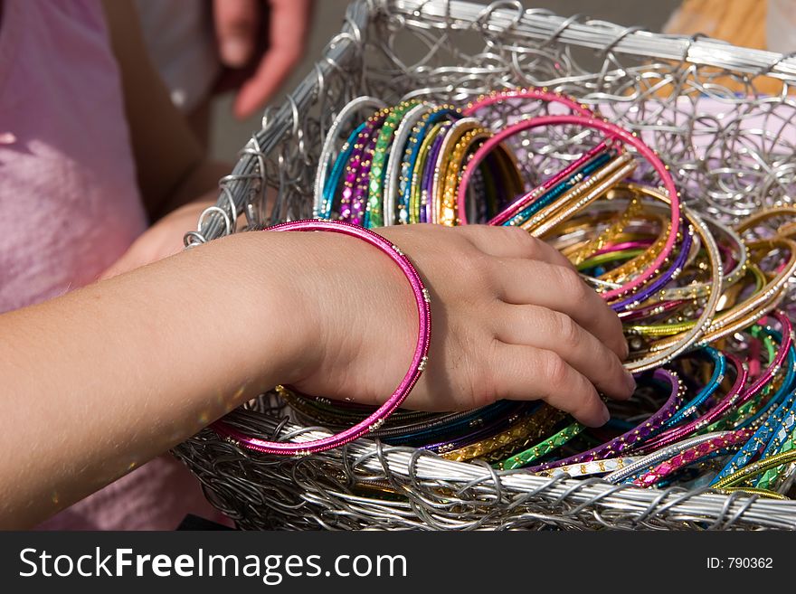 A young girl finds a basket of colorful bracelets and tries one on for size. A young girl finds a basket of colorful bracelets and tries one on for size.