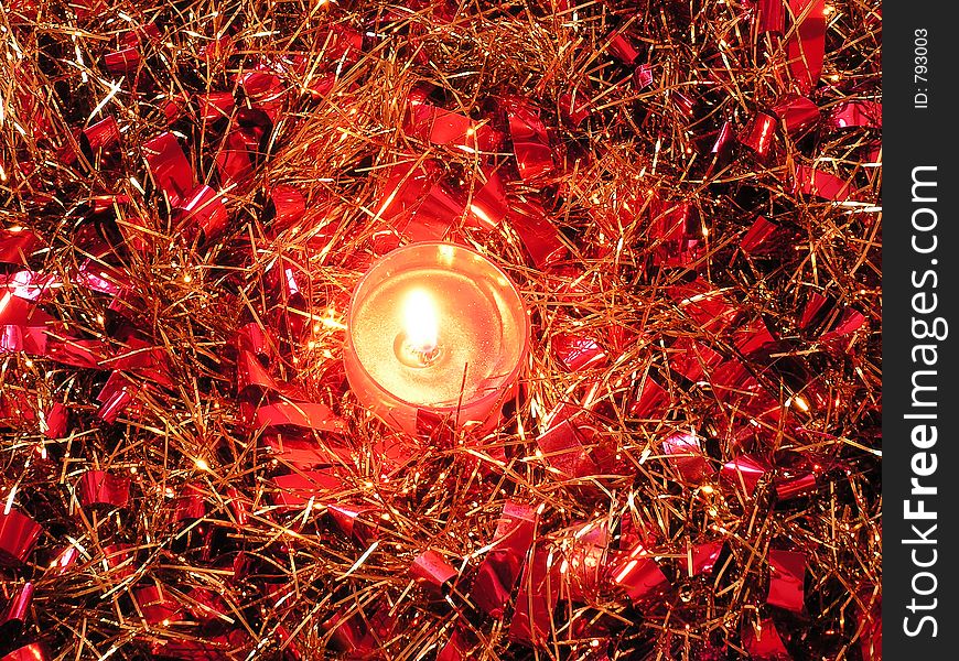 A scented candle in the centre of some swirled up red and gold tinsel. A scented candle in the centre of some swirled up red and gold tinsel.
