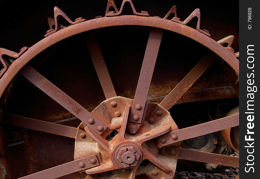 Old rusty steel wheel on ancient farming equipment showing triangle-shaped traction or tread devices.