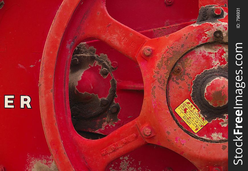 Steel crank wheel painted a bright red and covered in dirt on an old hay baling machine. Steel crank wheel painted a bright red and covered in dirt on an old hay baling machine.