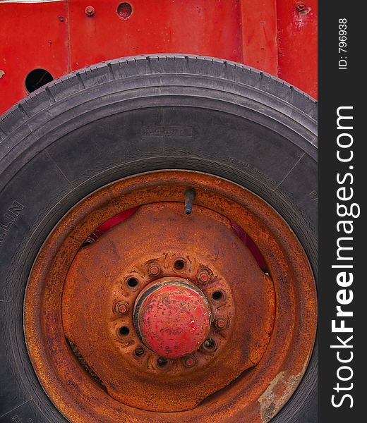 Old tire and wheel painted a bright red and covered in rust on an old hay baling machine.