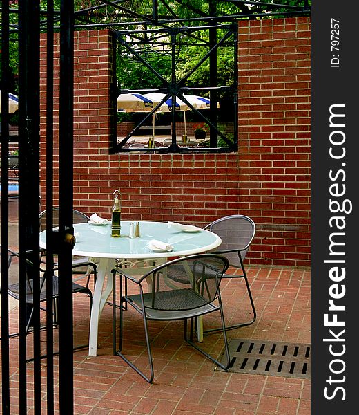 Secluded cyan dining table and chairs partially behind an iron gate at an outdoor cafe surrounded by red brick and green foliage.