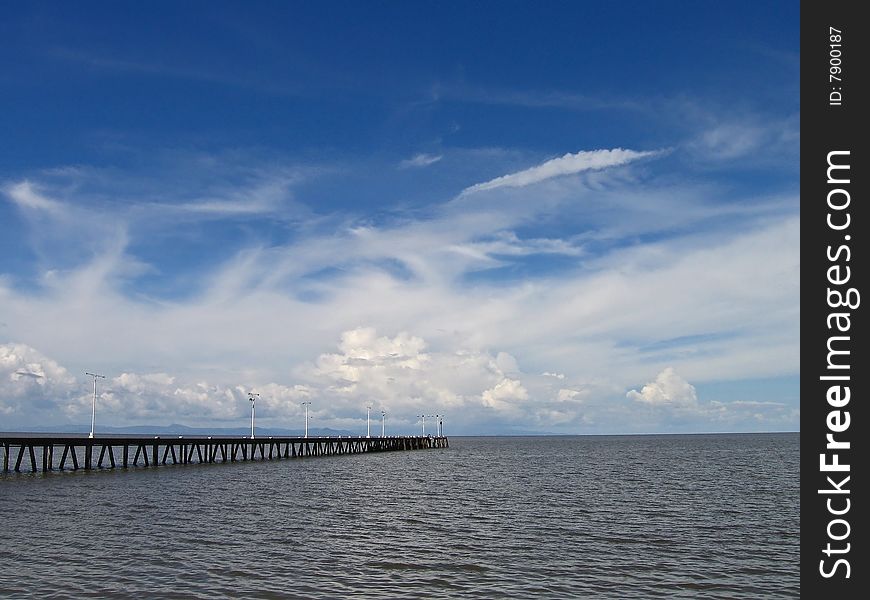 A long wooden dock on a lake with blue cloudy sky. A long wooden dock on a lake with blue cloudy sky