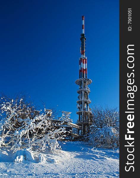 Transmitter of TV and radio signal, steel construction in winter landscape under snow cover.