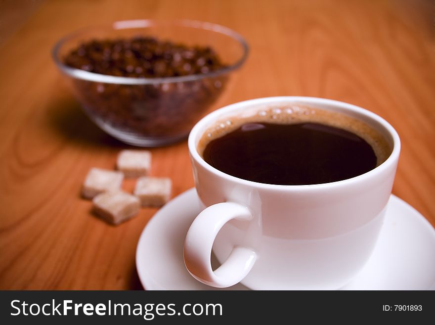 Cup of coffee, sugar and beans in glass bowl on wooden table