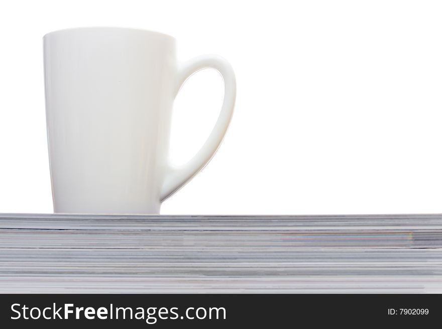 White cup on the heap of magazines isolated on white. White cup on the heap of magazines isolated on white.