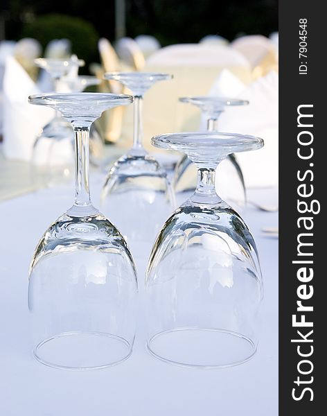 Two glasses upside down on a table. In the background and out of focus are more glasses and party tables decorated in white, gold and yellow.