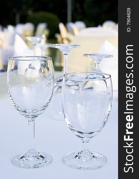 Two glasses on a table. In the background and out of focus are more glasses and party tables decorated in white, gold and yellow.