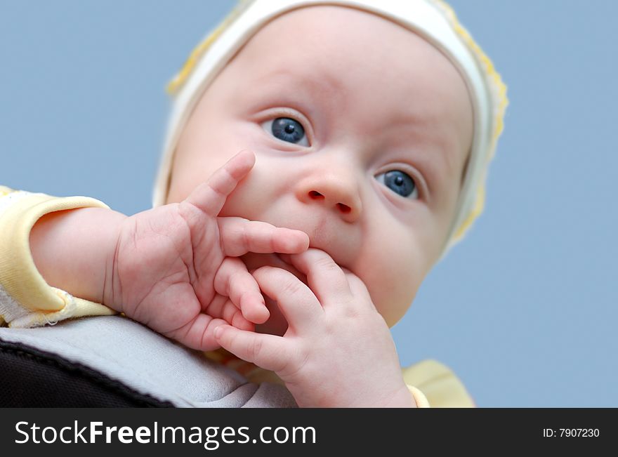 Little newbord boy with fingers in his mouth on blue background