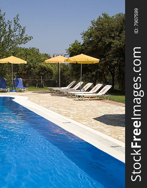 Sun loungers by a deep blue swimming pool. Sun loungers by a deep blue swimming pool