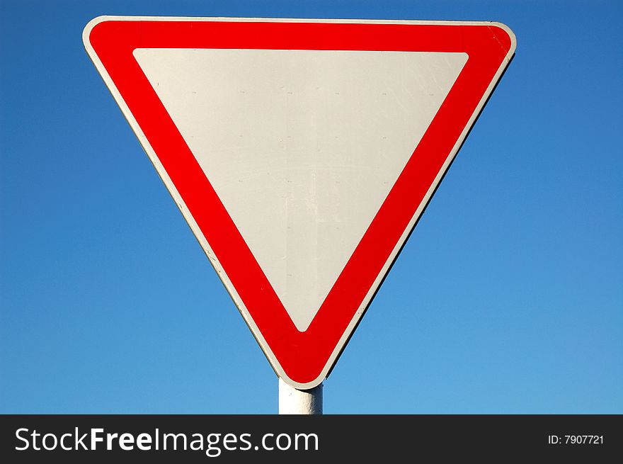 Give way sign closeup, isolated on blue sky