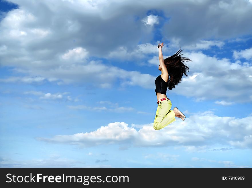 A young girl jumping in front of blue sky and clouds. A young girl jumping in front of blue sky and clouds