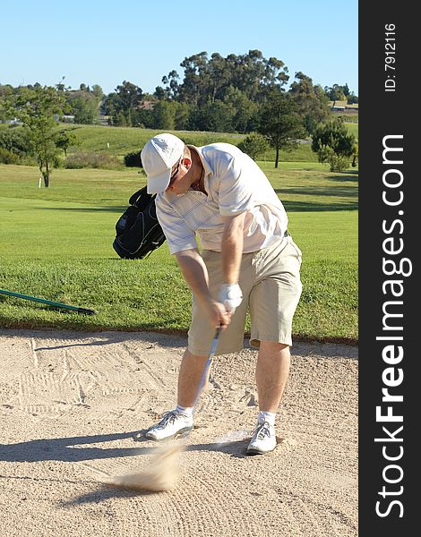 Young male golfer hitting the ball from the sand bunker on a beautiful summer day. Young male golfer hitting the ball from the sand bunker on a beautiful summer day