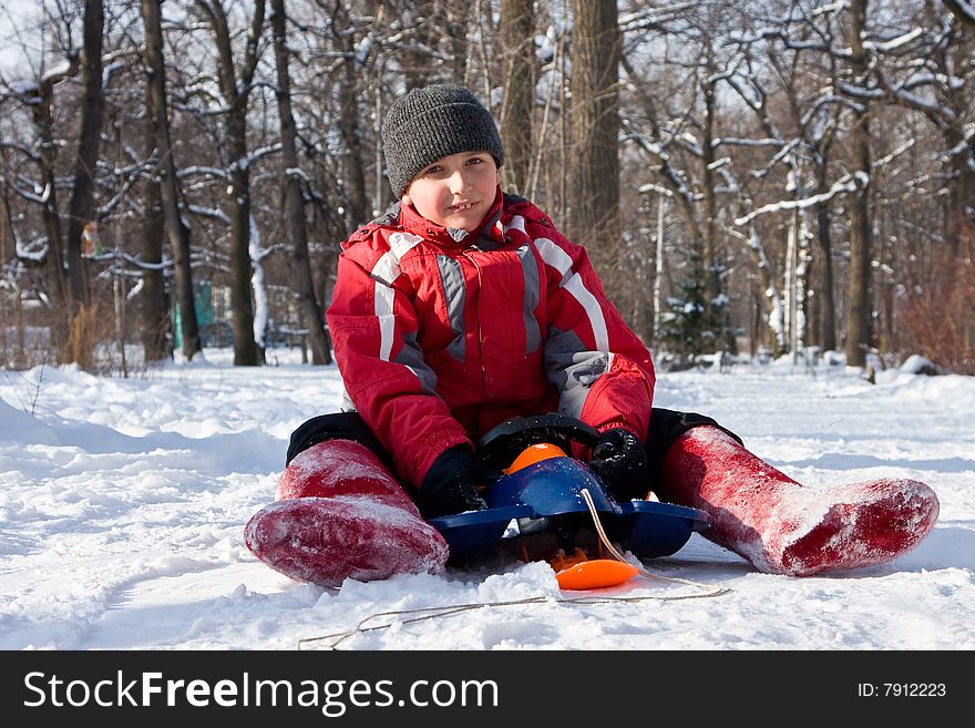 The boy sitting on a sledge in red valenki.