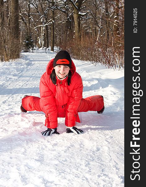 The girl in red overalls does gymnastics on snow.