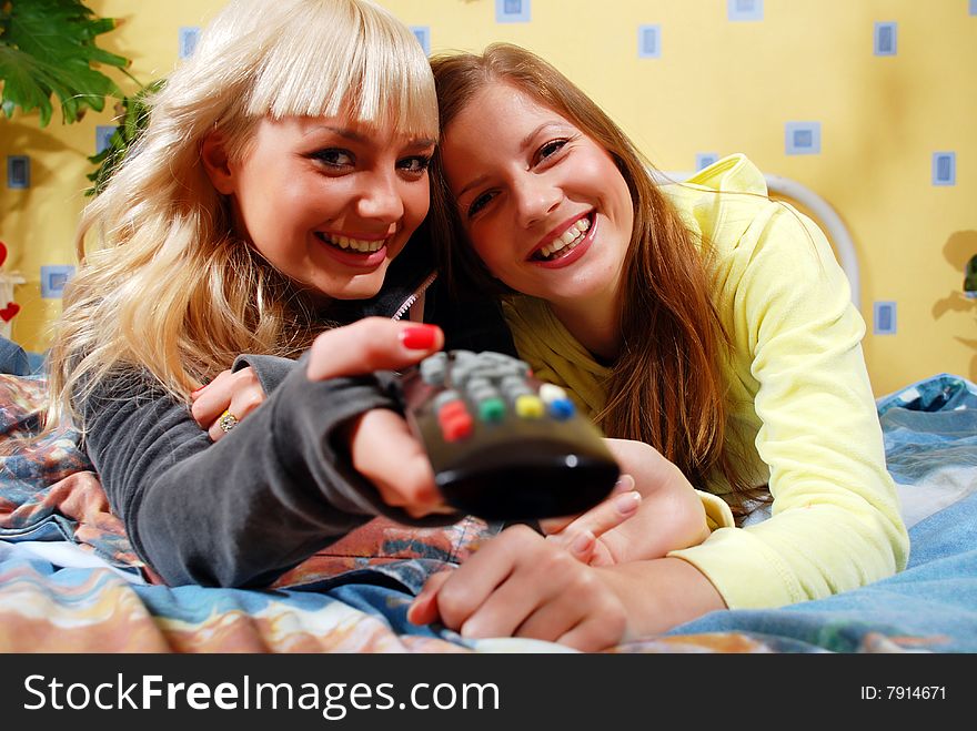 Two beautiful women watching television at the bedroom. Two beautiful women watching television at the bedroom