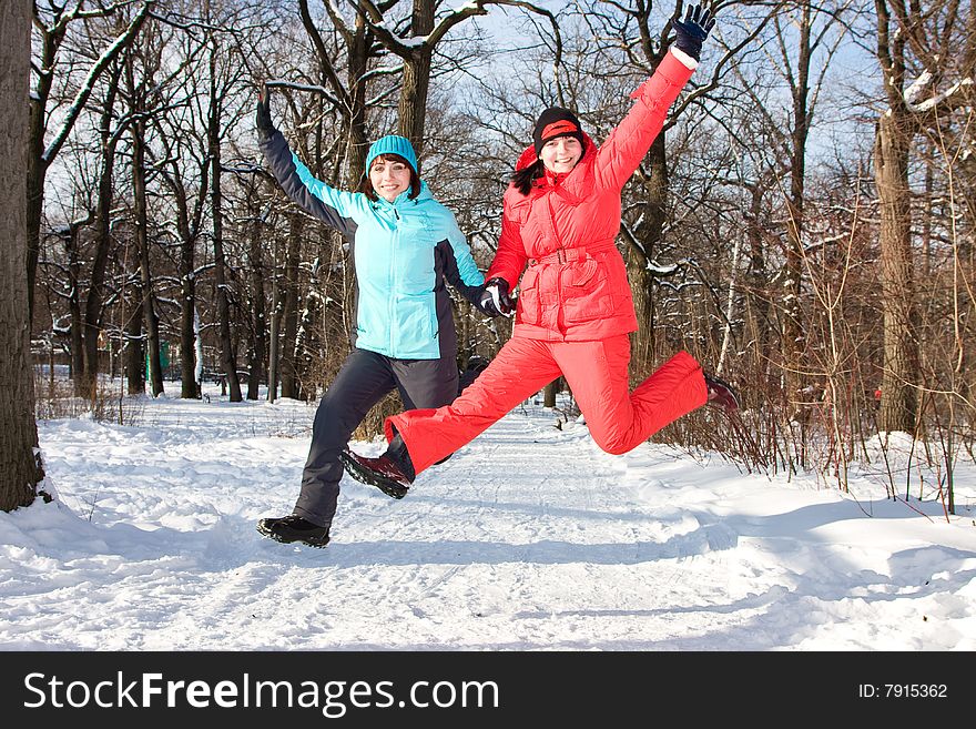 Two cheerful friendly girls jump in park in the winter.