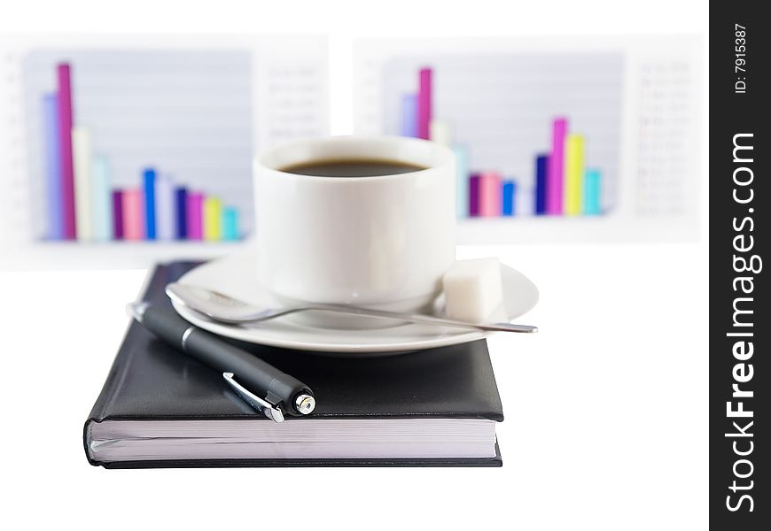 Coffee cup, standing on the black personal organizer, on a back background - two financial  diagrams . Focus at the pen. Isolated on white. Coffee cup, standing on the black personal organizer, on a back background - two financial  diagrams . Focus at the pen. Isolated on white.