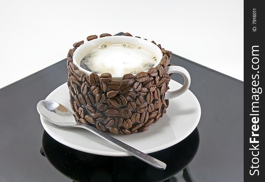 The coffee cup , original decorated by coffee grains(beans) on black plate. Isolated on white. The coffee cup , original decorated by coffee grains(beans) on black plate. Isolated on white.