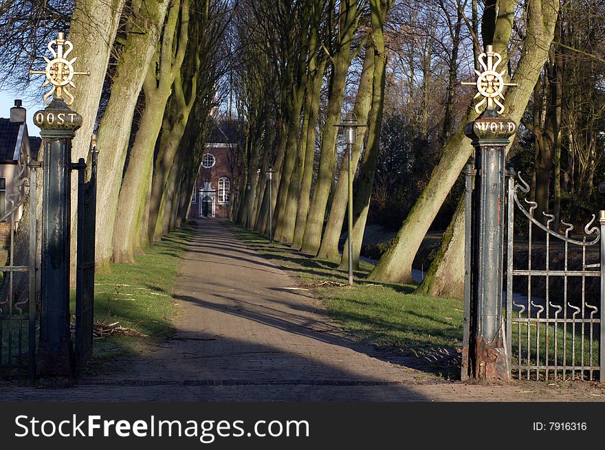 Composition with an old gilded iron gateway and the straight and narrow path between crooked tree which leads to an old Dutch church in northern Holland. Composition with an old gilded iron gateway and the straight and narrow path between crooked tree which leads to an old Dutch church in northern Holland.