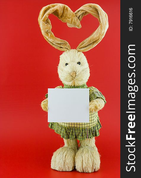 Straw hare with ears in the form of heart on a red background with the white nameplate. Straw hare with ears in the form of heart on a red background with the white nameplate.