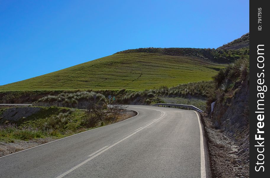 Road in early spring, green hill, blue sky