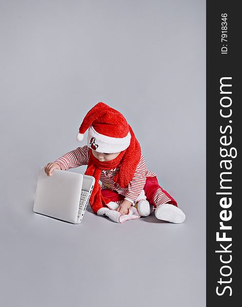 Baby santa claus with white laptop in grey background