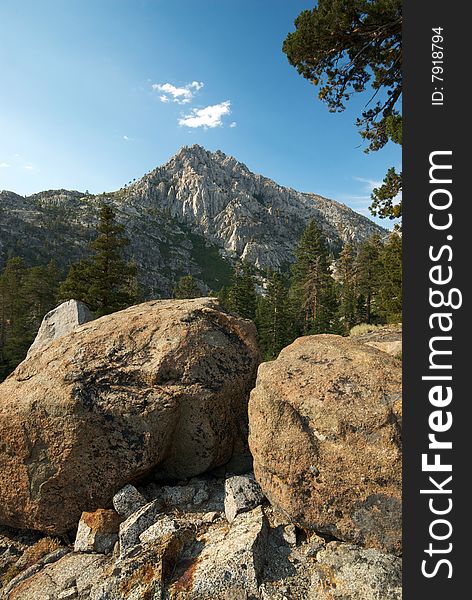 A towering mountain peak is framed by foreground boulders and a lush forest between them. A towering mountain peak is framed by foreground boulders and a lush forest between them