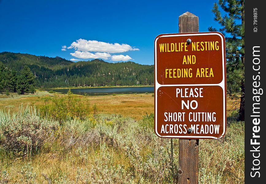 A scenic view of a pristine lake, mountains and forest with a sign to protect the wildlife. A scenic view of a pristine lake, mountains and forest with a sign to protect the wildlife