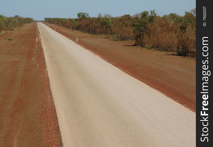 High angle shot of an Australian country road with red dirt road-side and shrubby surrounding countryside. Australia.