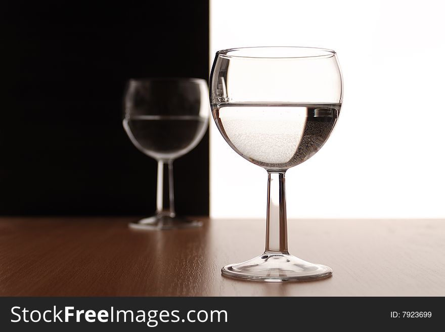 Two wine glasses in backlight on white and black contrast background
