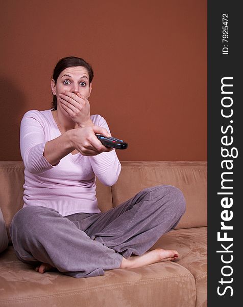 A young woman sits in front of a TV with the remote control in her hand on a couch. A lot of copyspace left. She seems to be afraid. A young woman sits in front of a TV with the remote control in her hand on a couch. A lot of copyspace left. She seems to be afraid.