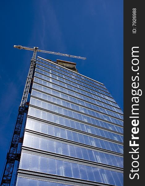 A blue glass high rise tower with a white crane on a bright blue sky. A blue glass high rise tower with a white crane on a bright blue sky