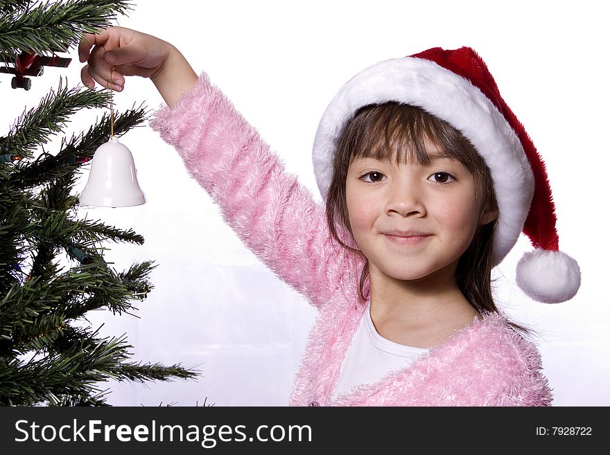 A young girl holds a small bell ornament next to a christmas tree. A young girl holds a small bell ornament next to a christmas tree.