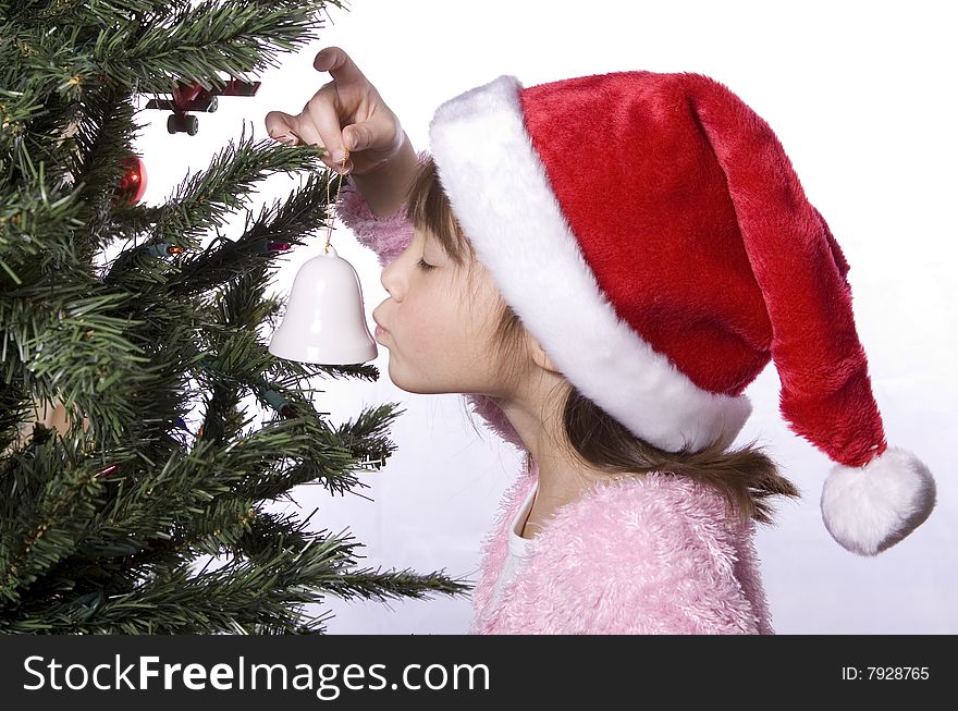A young girl kisses a small bell ornament next to a christmas tree. A young girl kisses a small bell ornament next to a christmas tree.