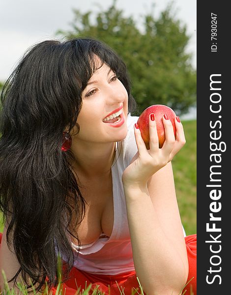 Pretty woman eating red apple on the summer glade