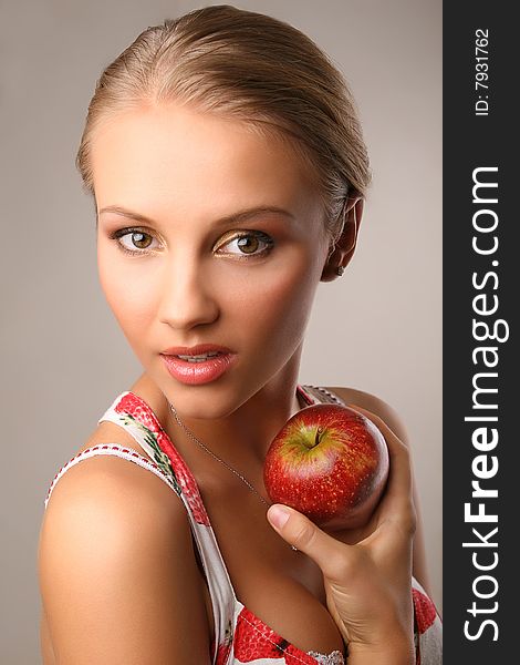 Portrait of attractive young woman holding red apple and looking at camera