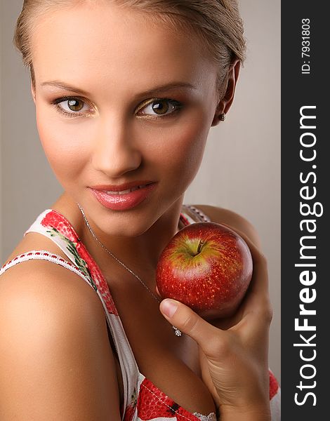 Portrait of attractive young woman holding red apple and looking at camera