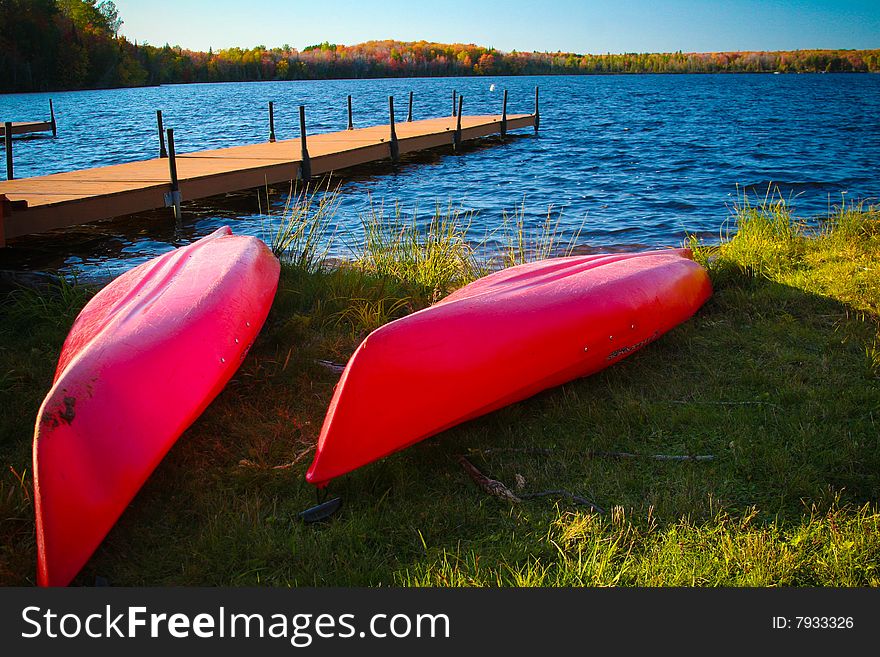 Red kayaks on lake shore with dock in background. Red kayaks on lake shore with dock in background