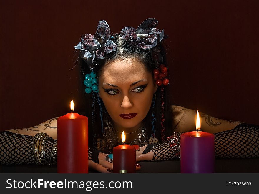 Young beautiful soothsayer with three candles on dark red background