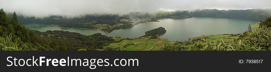 Green and Blue Lagoons of Sete Cidades under heavy low clouds. Pastures and Sete Cidades village. Azores, Portugal. Green and Blue Lagoons of Sete Cidades under heavy low clouds. Pastures and Sete Cidades village. Azores, Portugal