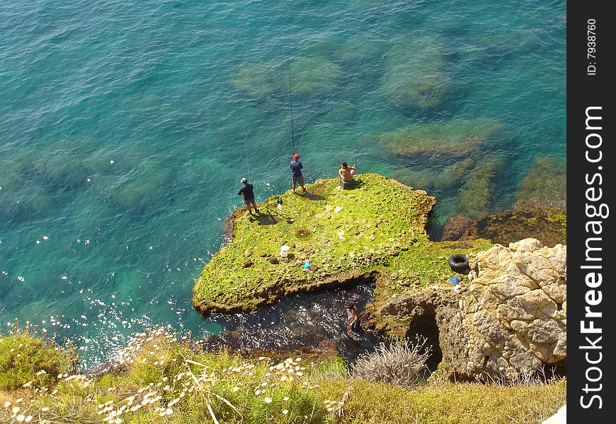 A shot from an eagle eye view of a top of a rock towards fishermen. A shot from an eagle eye view of a top of a rock towards fishermen