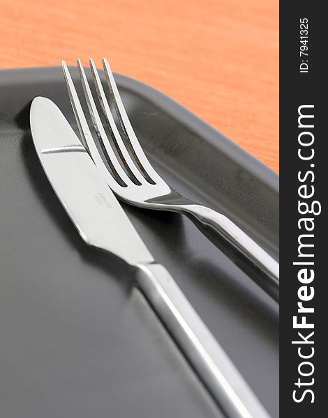 Detail of a knife and fork at a black dinner plate with a orange background. Detail of a knife and fork at a black dinner plate with a orange background