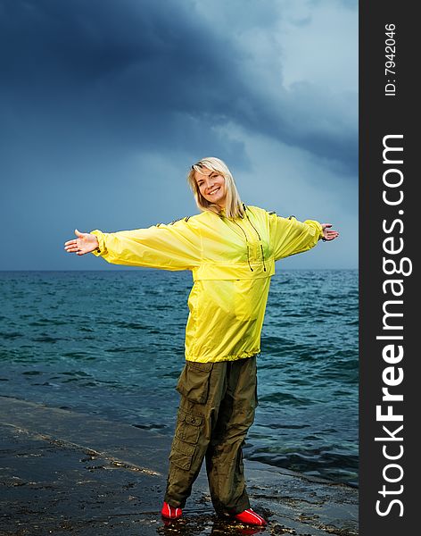 Young woman in yellow raincoat near the ocean at storm