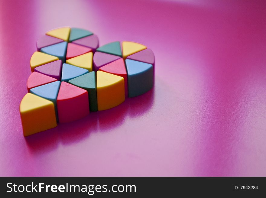 Heart made of small pieces , yellow blue purple green and orange on light background