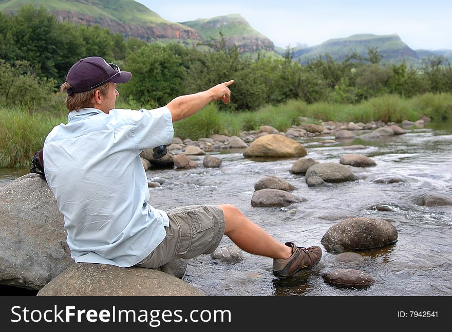 Young man sitting on rock pointing